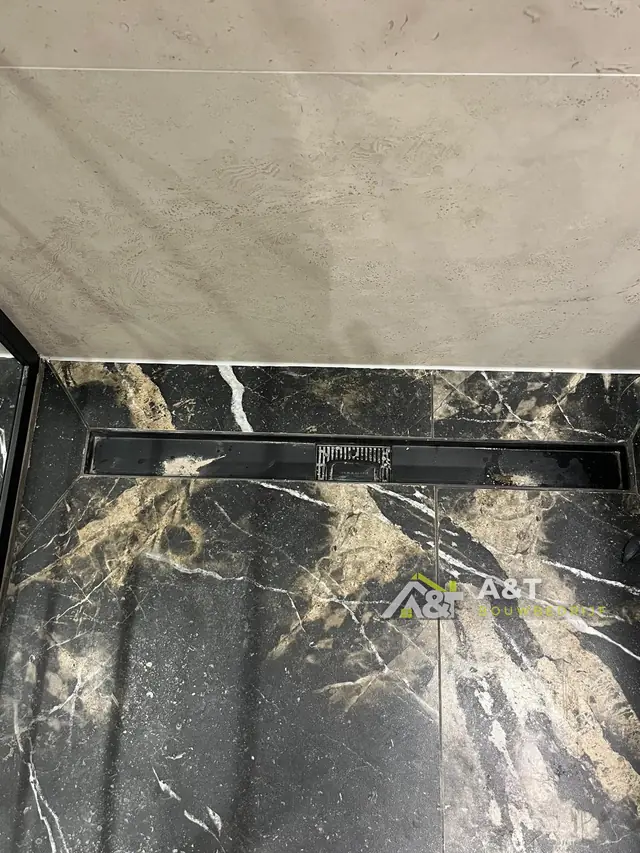 Douchegoot in zwart marmer. Vloer in zwart-goud marmerlook met een lange douchegoot.