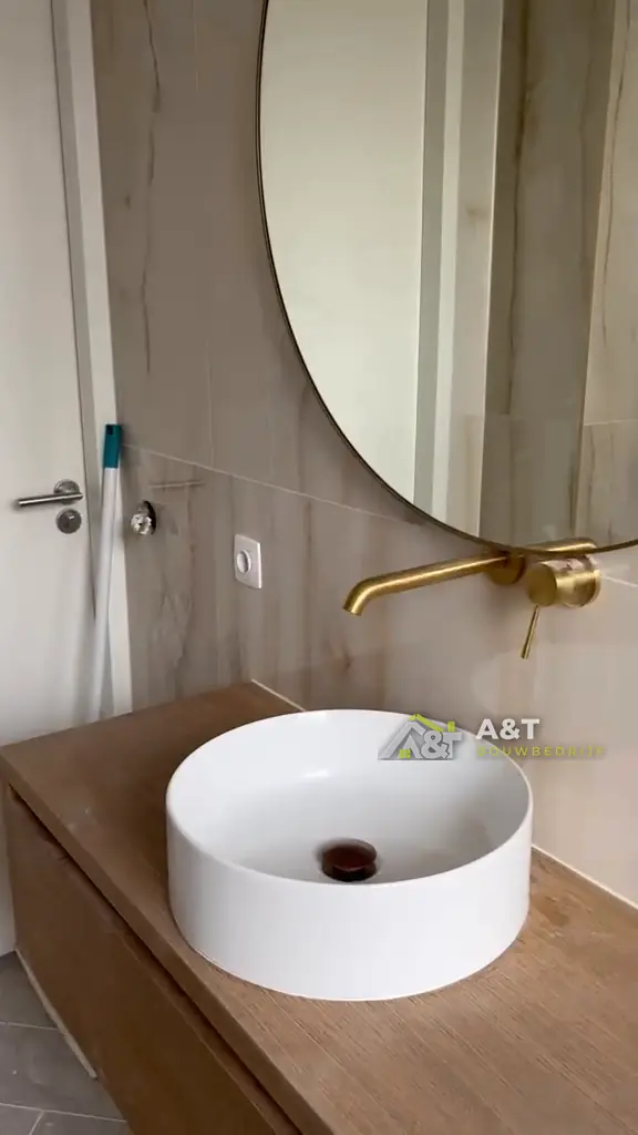 Waskom met gouden kraan. Ronde spiegel, gouden wandkraan en een waskom op houten blad.